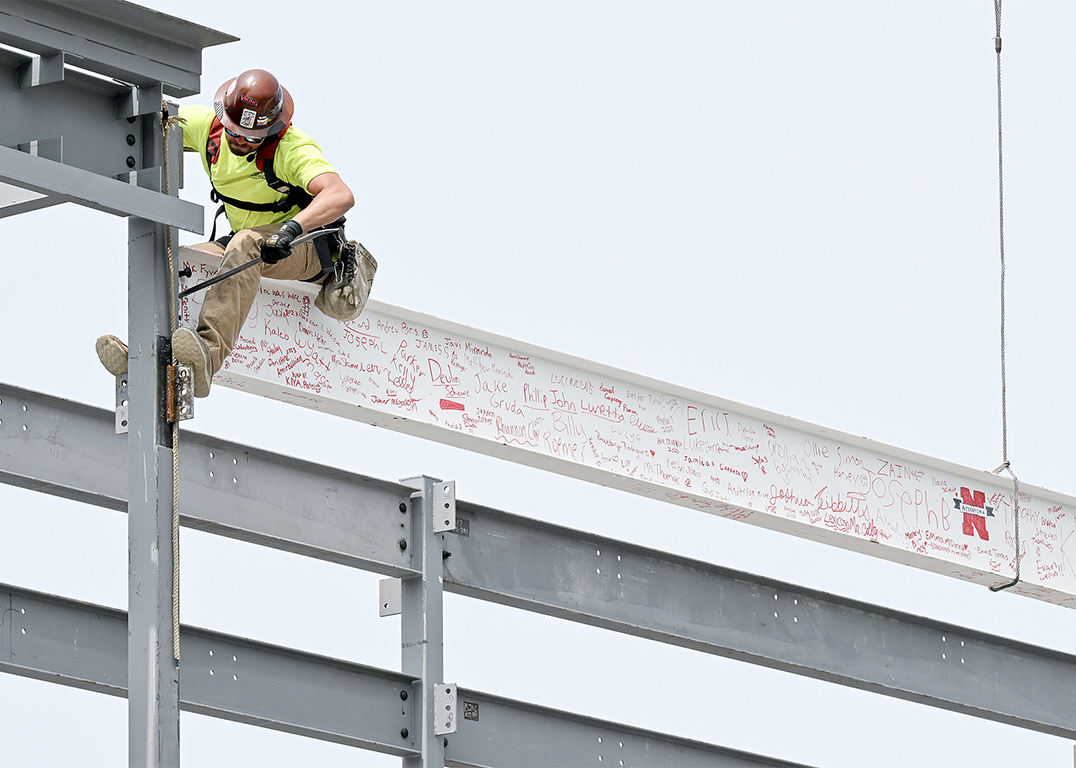 A construction worker secures a steel beam marked by children's' writing into place.