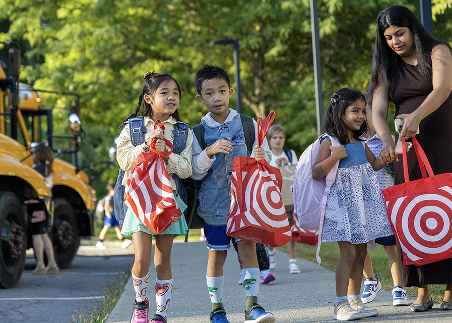 Young children carrying Target shopping bags walking together outside near a school bus.