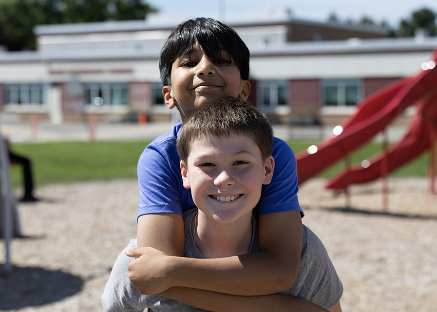 Two children smiling while playing together outdoors on a school playground.