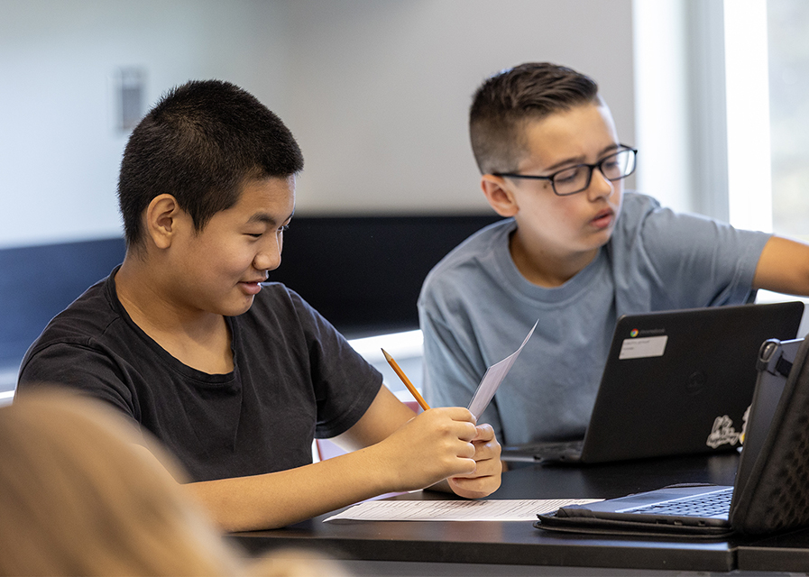 Two students working at a desk in a classroom.