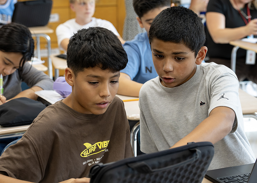 Two students view a laptop screen together.