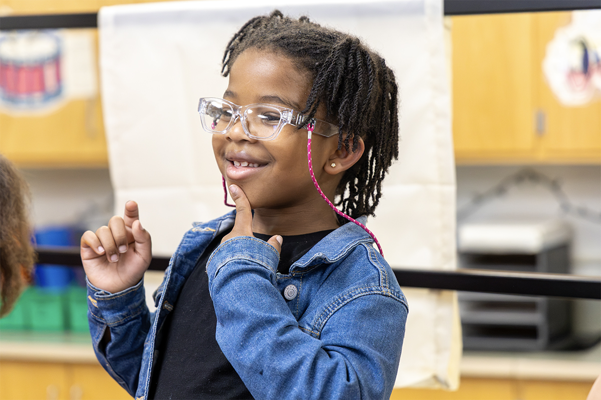 elementary student singing and smiling and pointing at chin