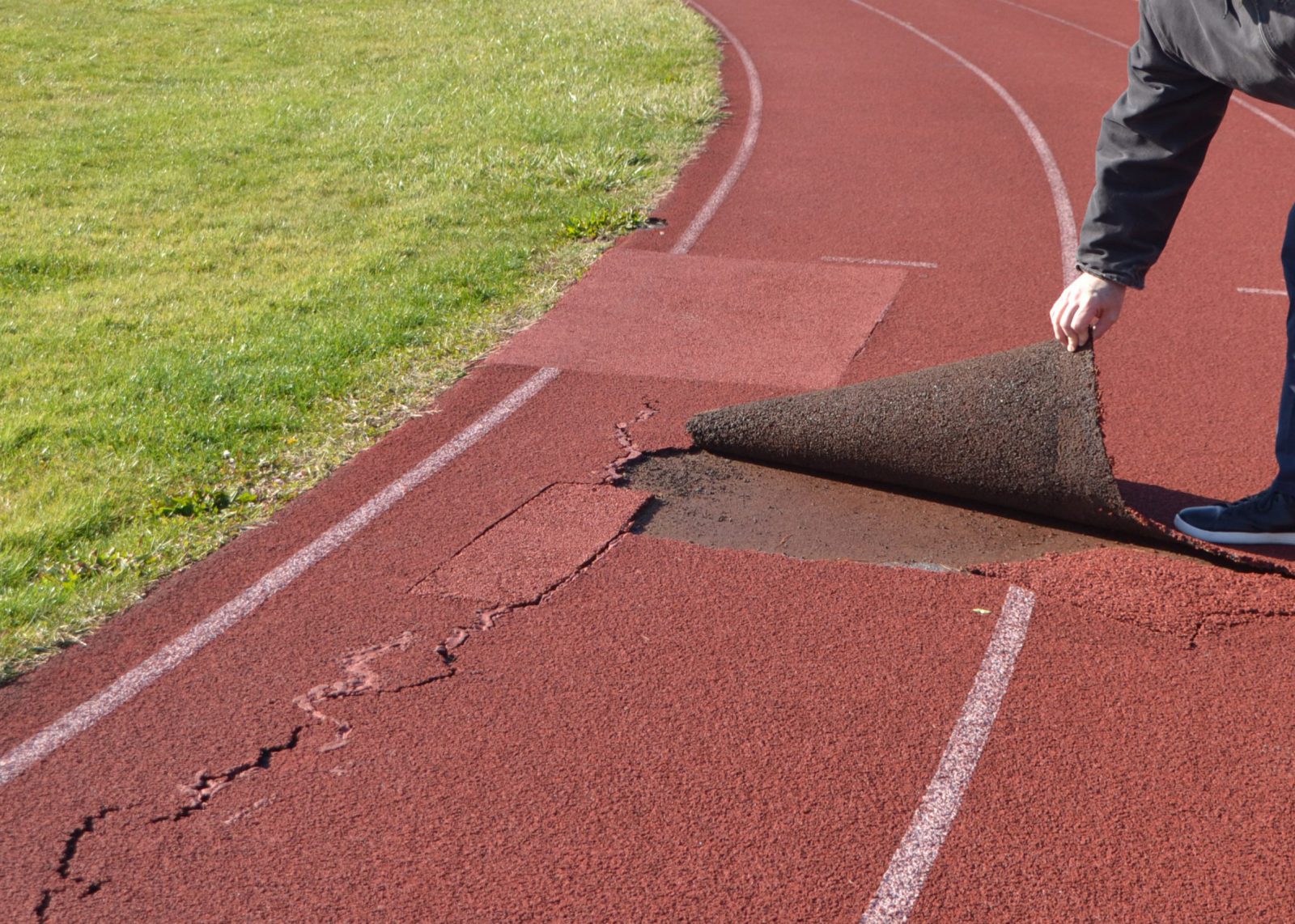 Image of the high school track with someone peeling up the top layer of it
