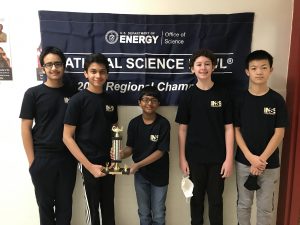 The students on the Van Antwerp Science Bowl Team stand side by with two students at the center holding a trophy.