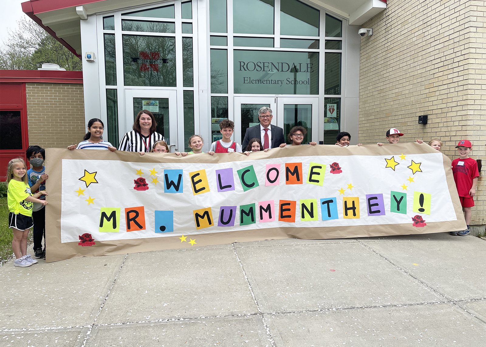 group of students with principal and superintendent with sign that read welcome mr. mummenthey