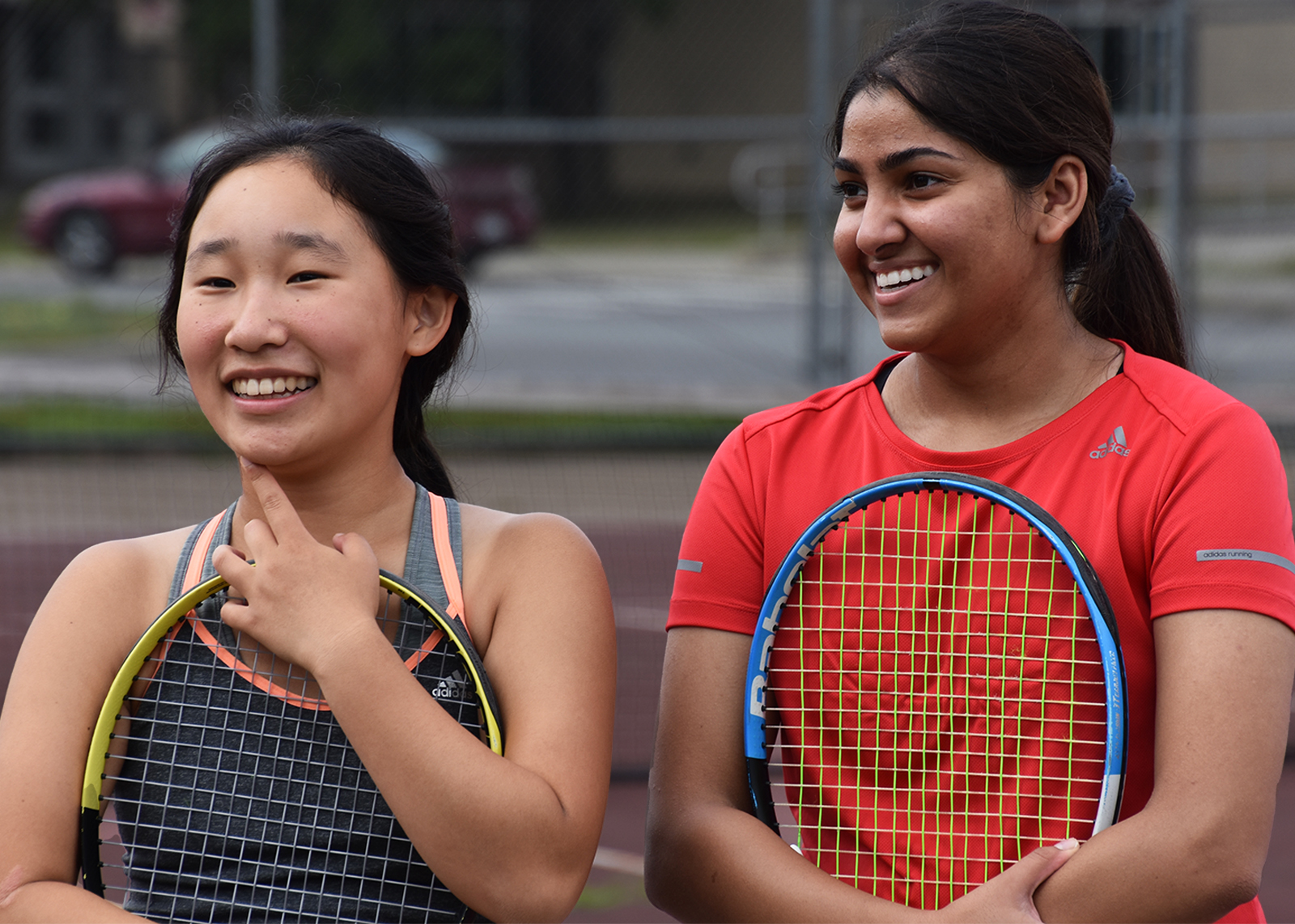 two female student athletes smiling holding tennis raquets