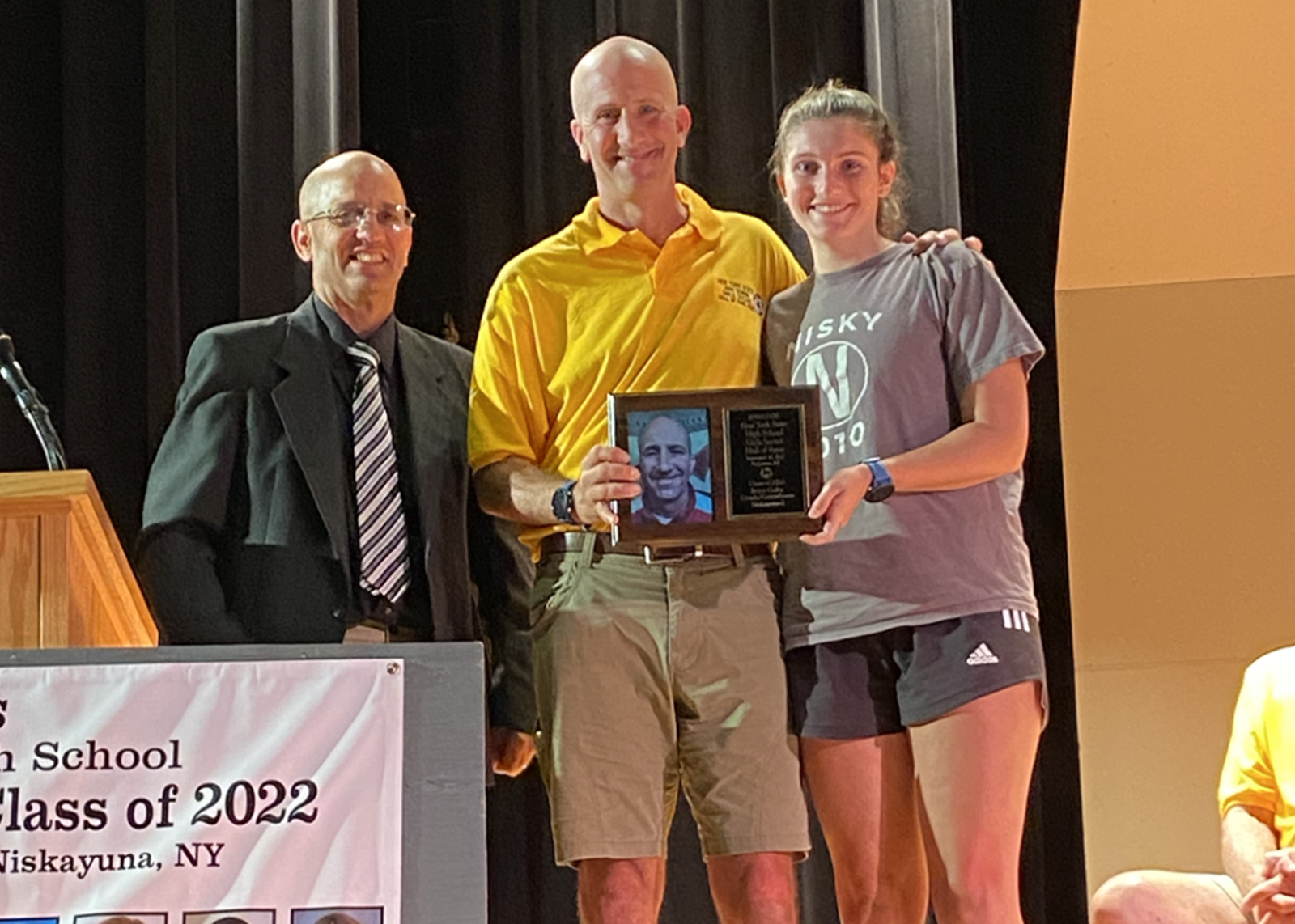 Soccer coach holding plaque with player and colleague around him