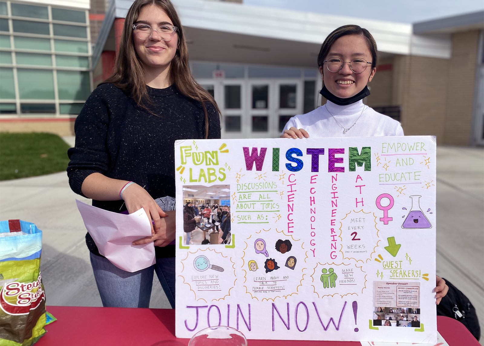 two students at an activities fair table holding a sign that says WISTEM