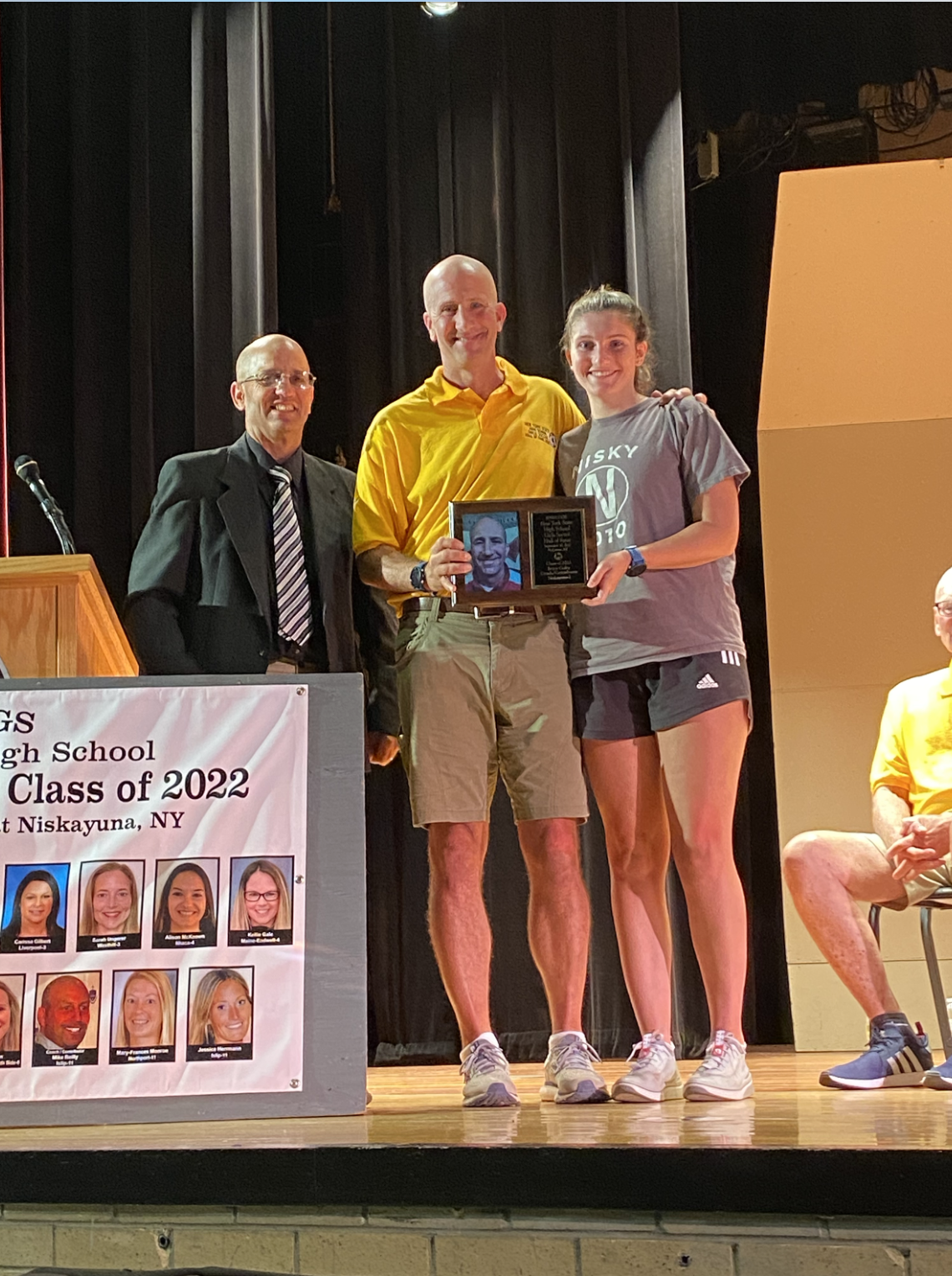 coach holding plaque with player on one side and colleague on the other