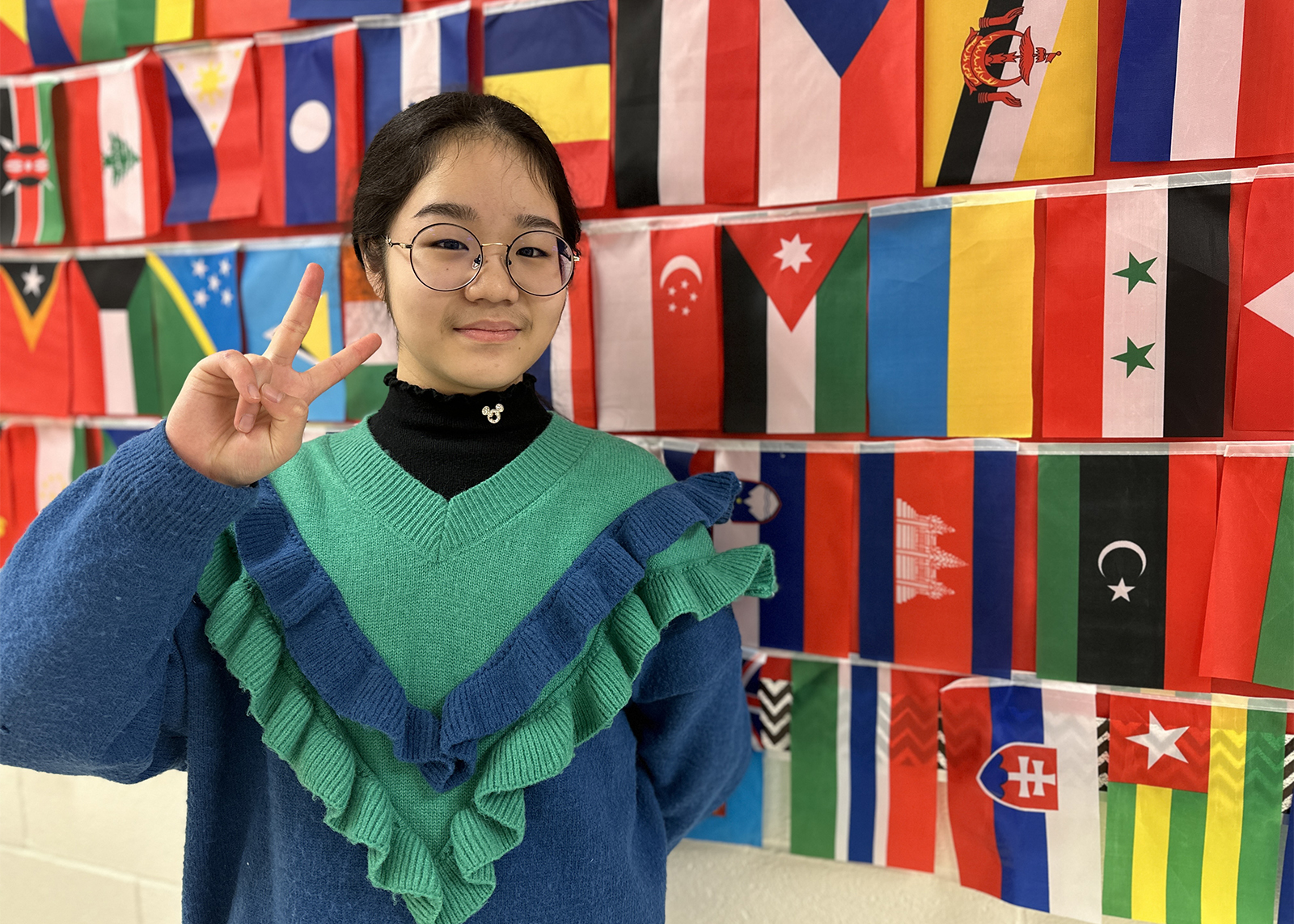 student giving the peace sign in front of a wall of flags