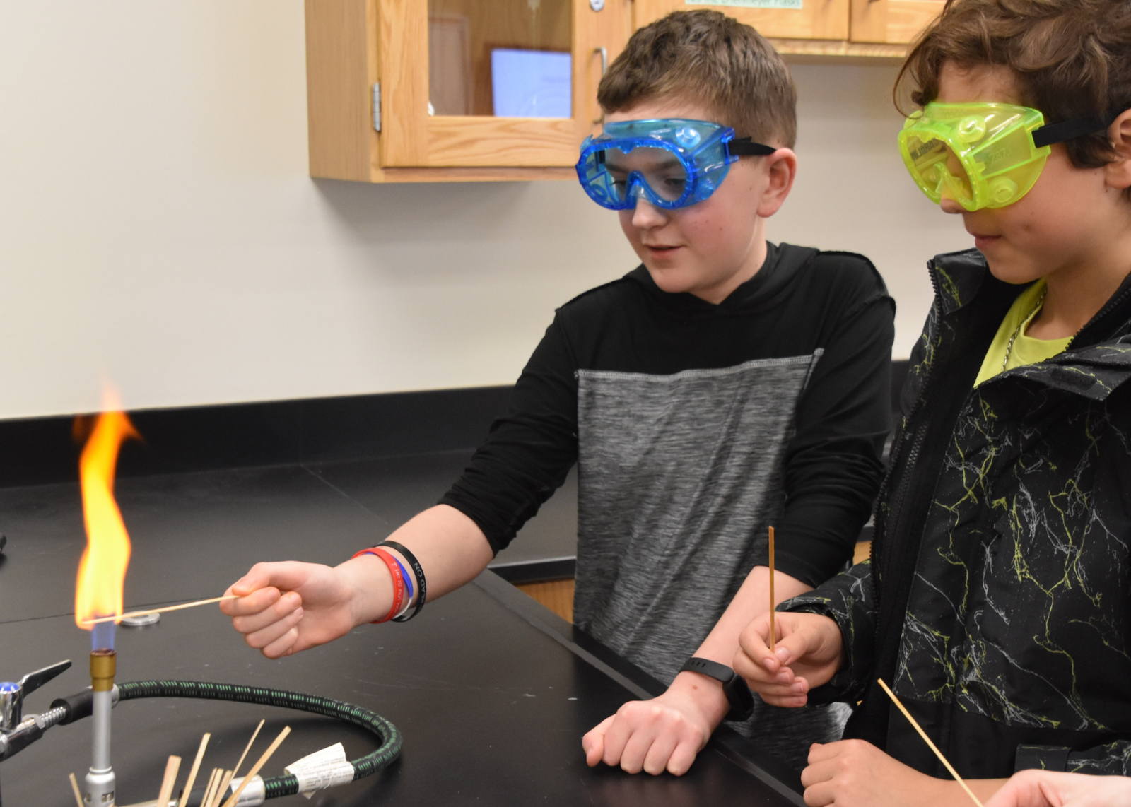 two students holding test strips over a bunsen burner wearing goggles