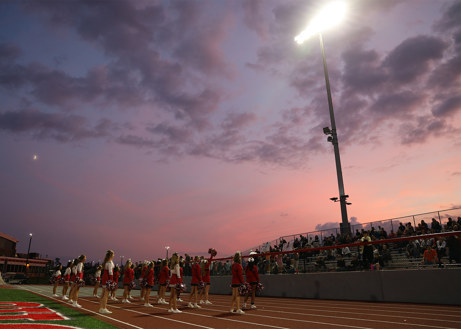sunset sky behind bleachers at football game with cheerleaders in forground