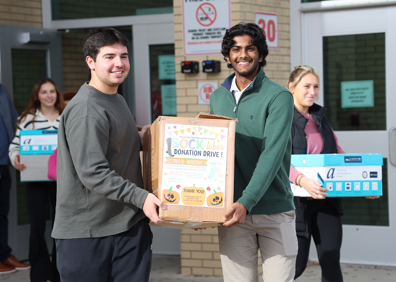 two students carry boxes of socks out to city mission truck