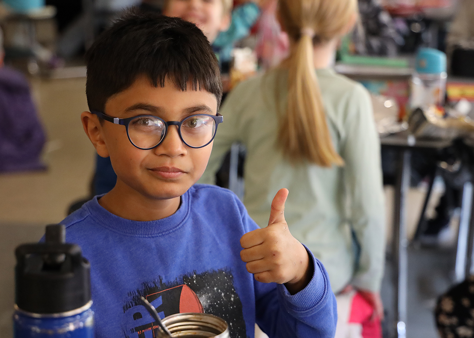student with glasses gives camera thumbs up