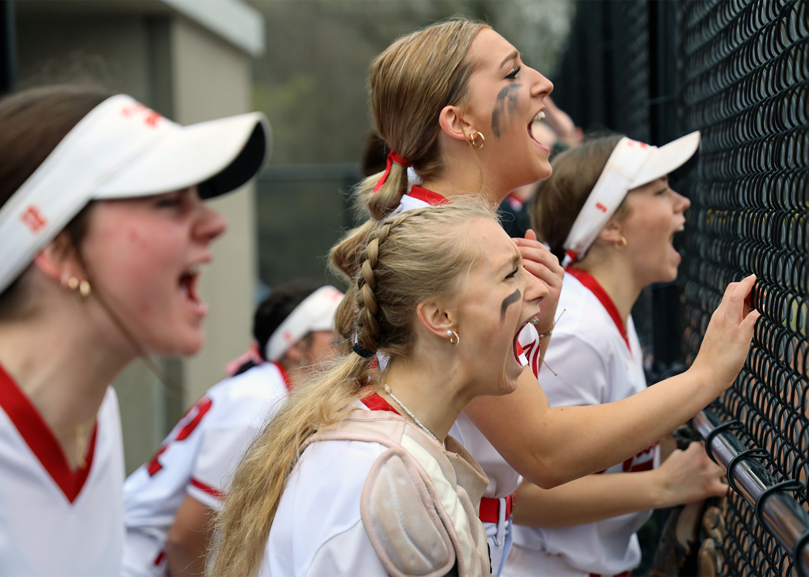 Softball teammates cheer while standing along fence