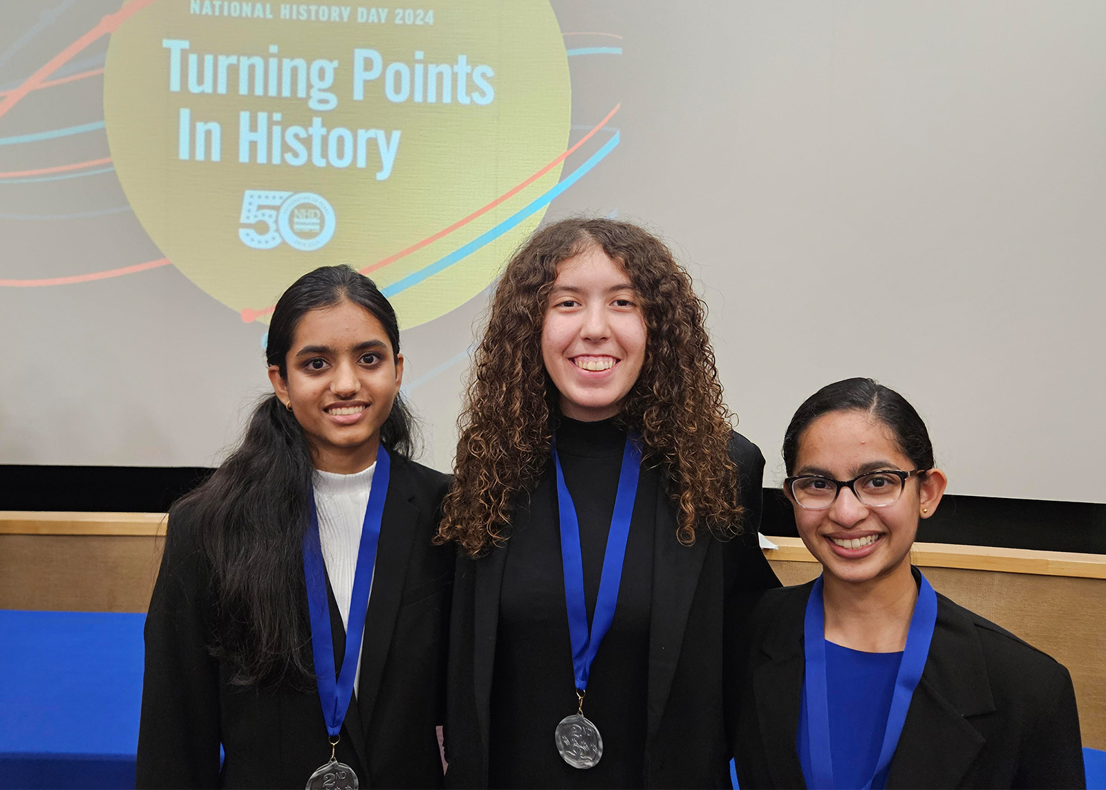 Three student sin black blazers wear their medals on blue lanyards