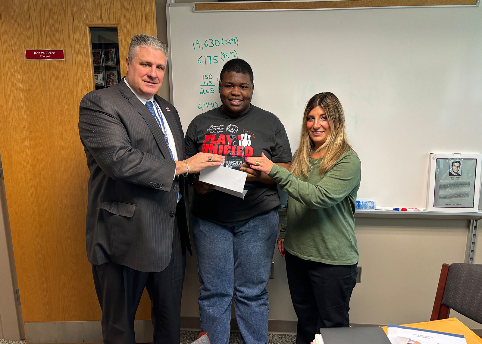 Two adults presenting a glass award to a student