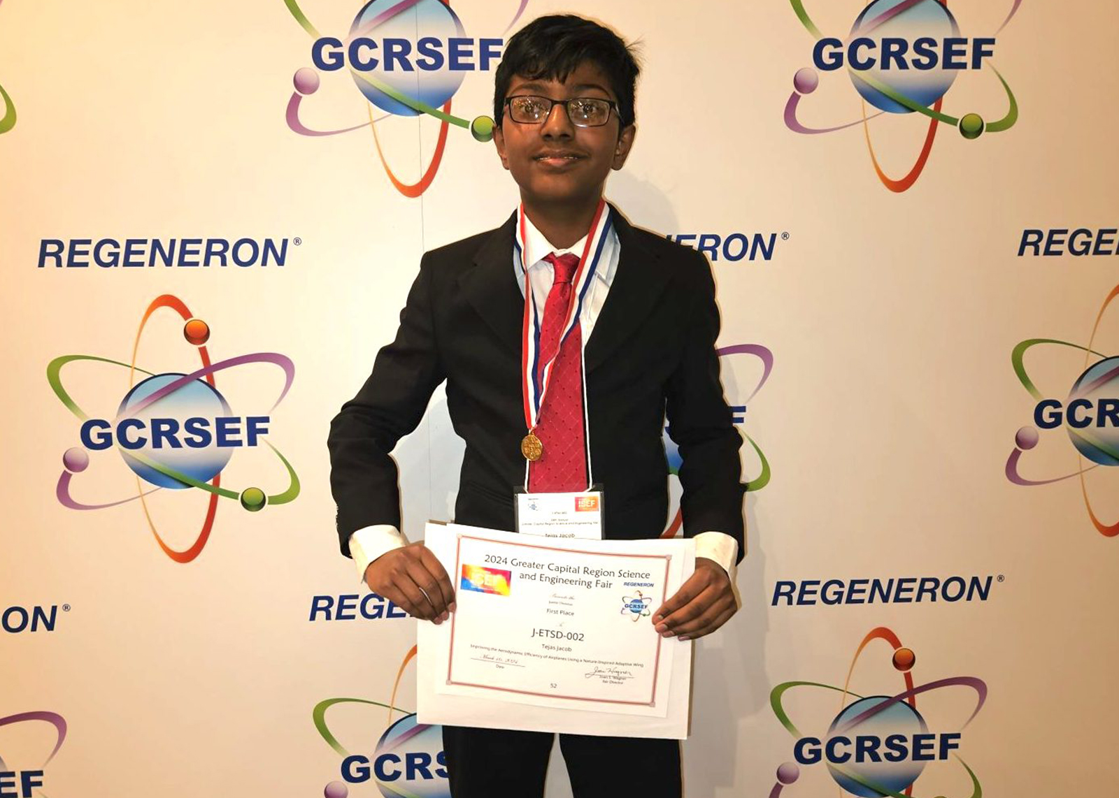 A student in a suit and tie displays a certificate and medal