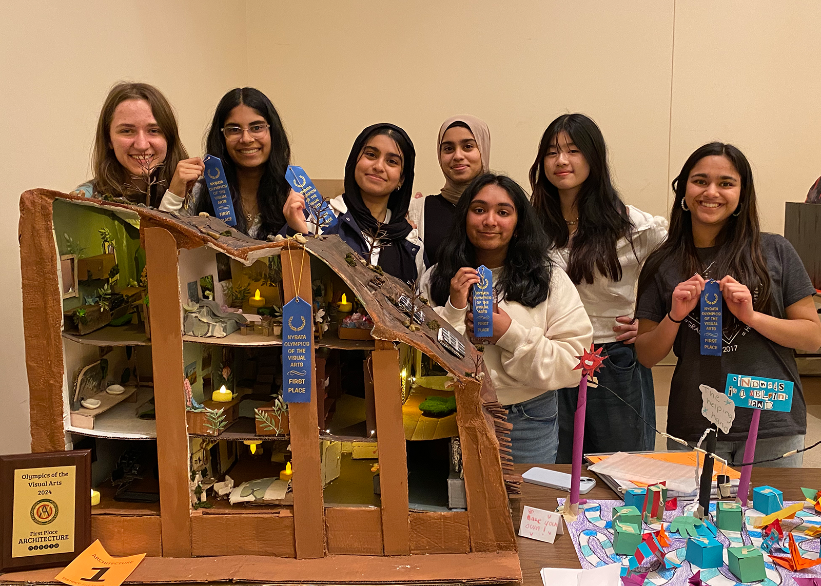 Several students pose with ribbons front of a 3D dollhouse