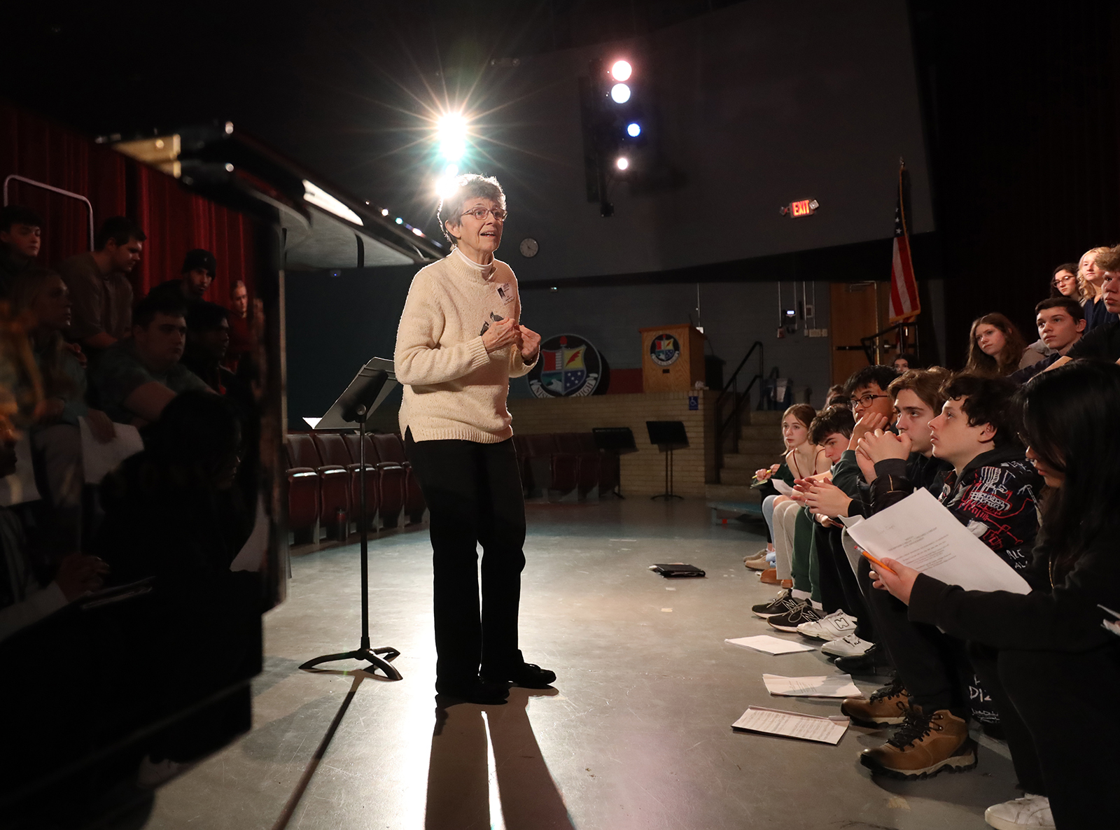 Phyllis Pulver stands on stage between crowds of Niskayuna High School students