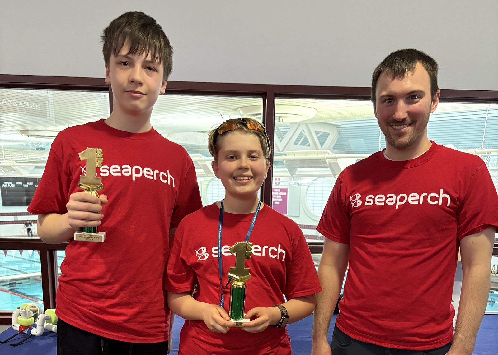 two students and a SeaPerch advisor smiling with trophies