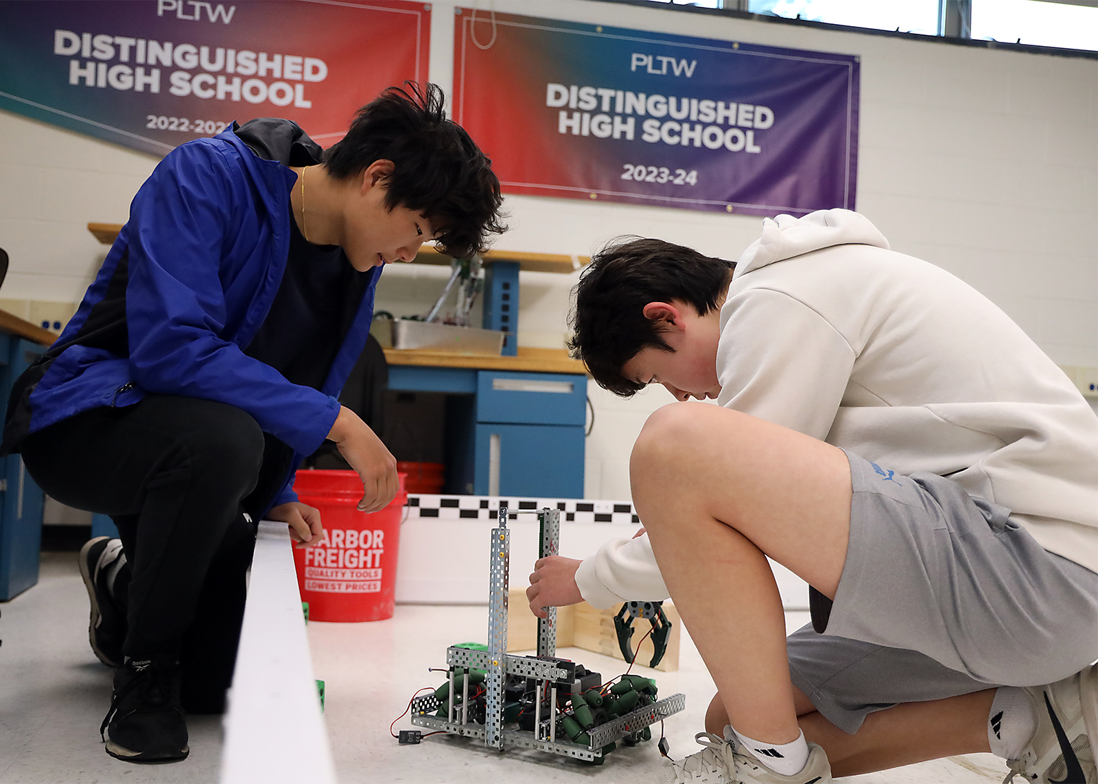 two students work on robot with project lead the way banners behind them