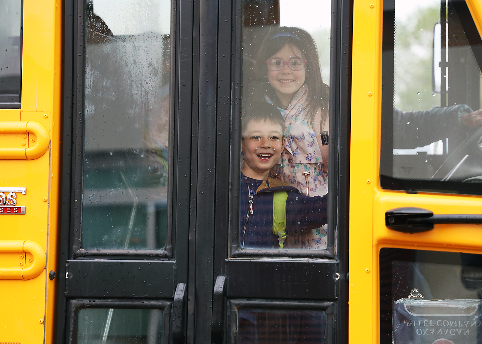 elementary students smiling behind closed bus door