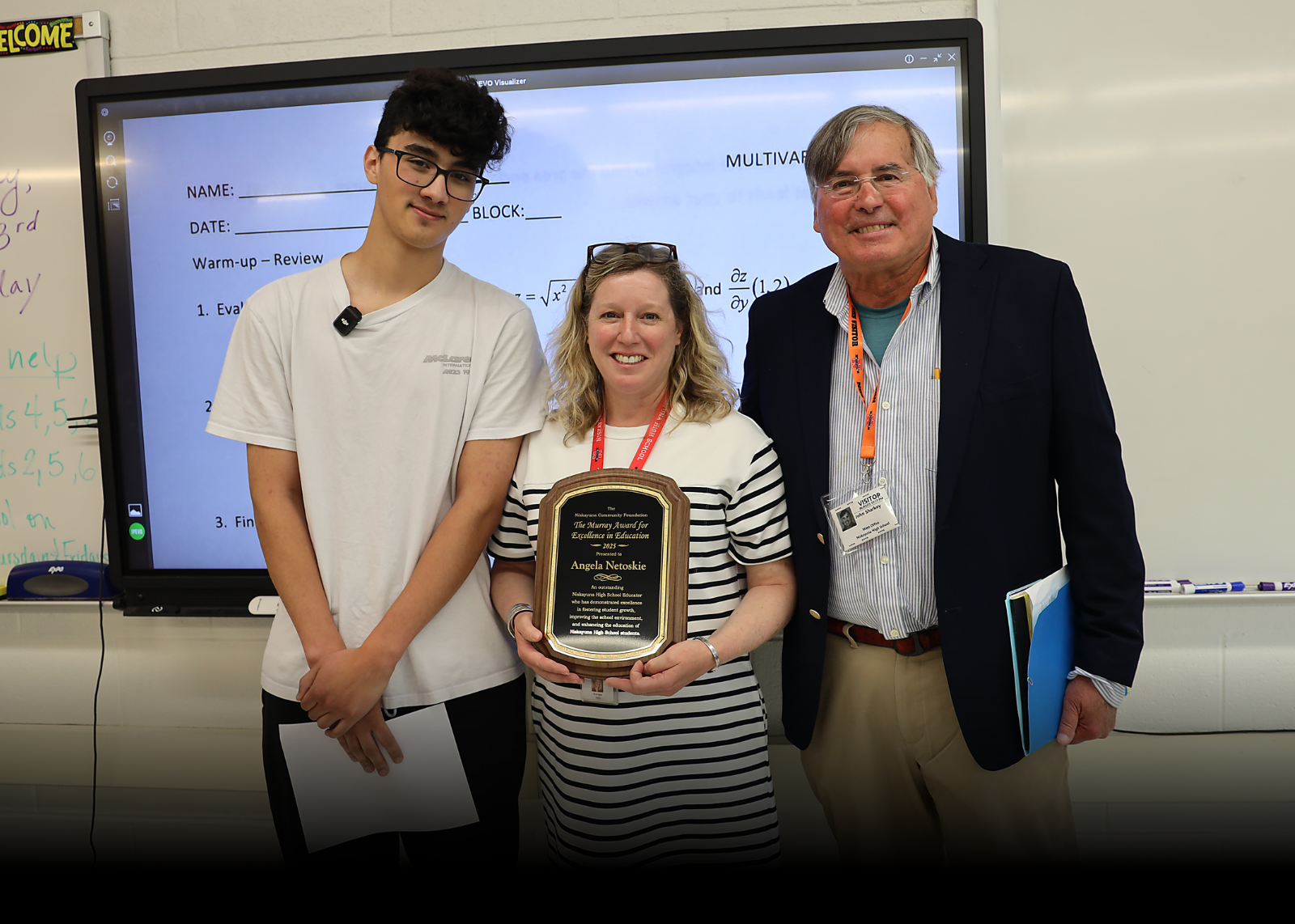 teacher holding plaque with student and presenter