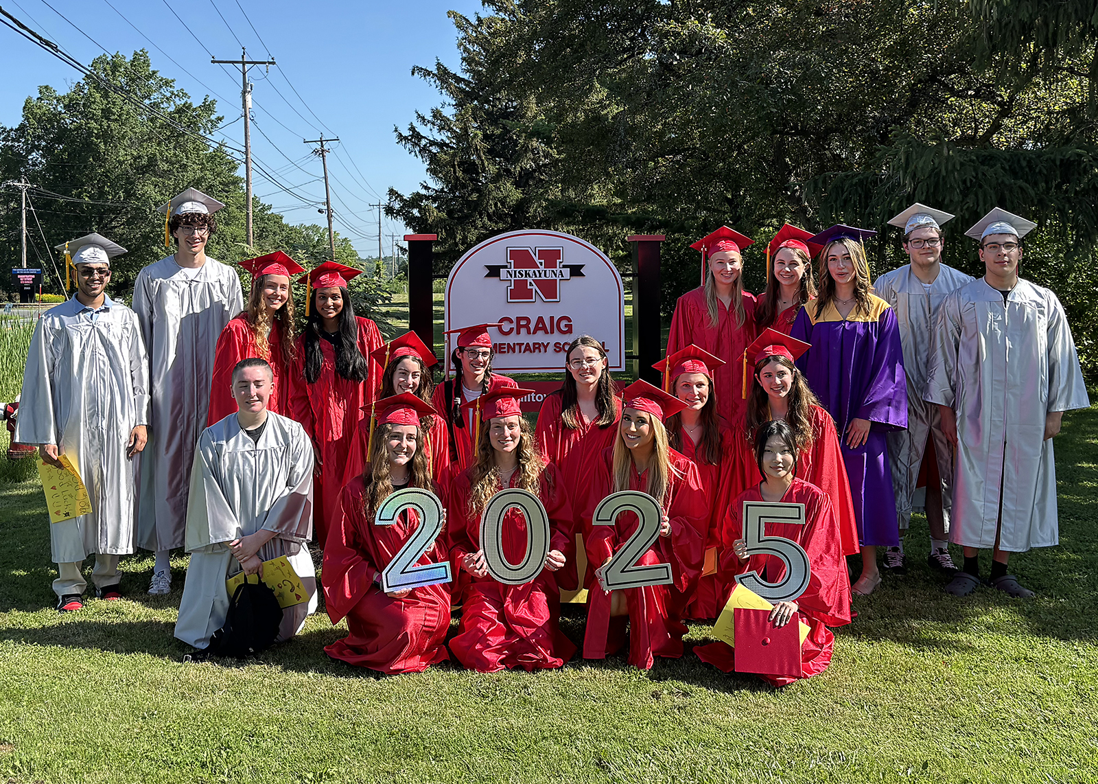 high school seniors in caps and gowns in front of elementary sign