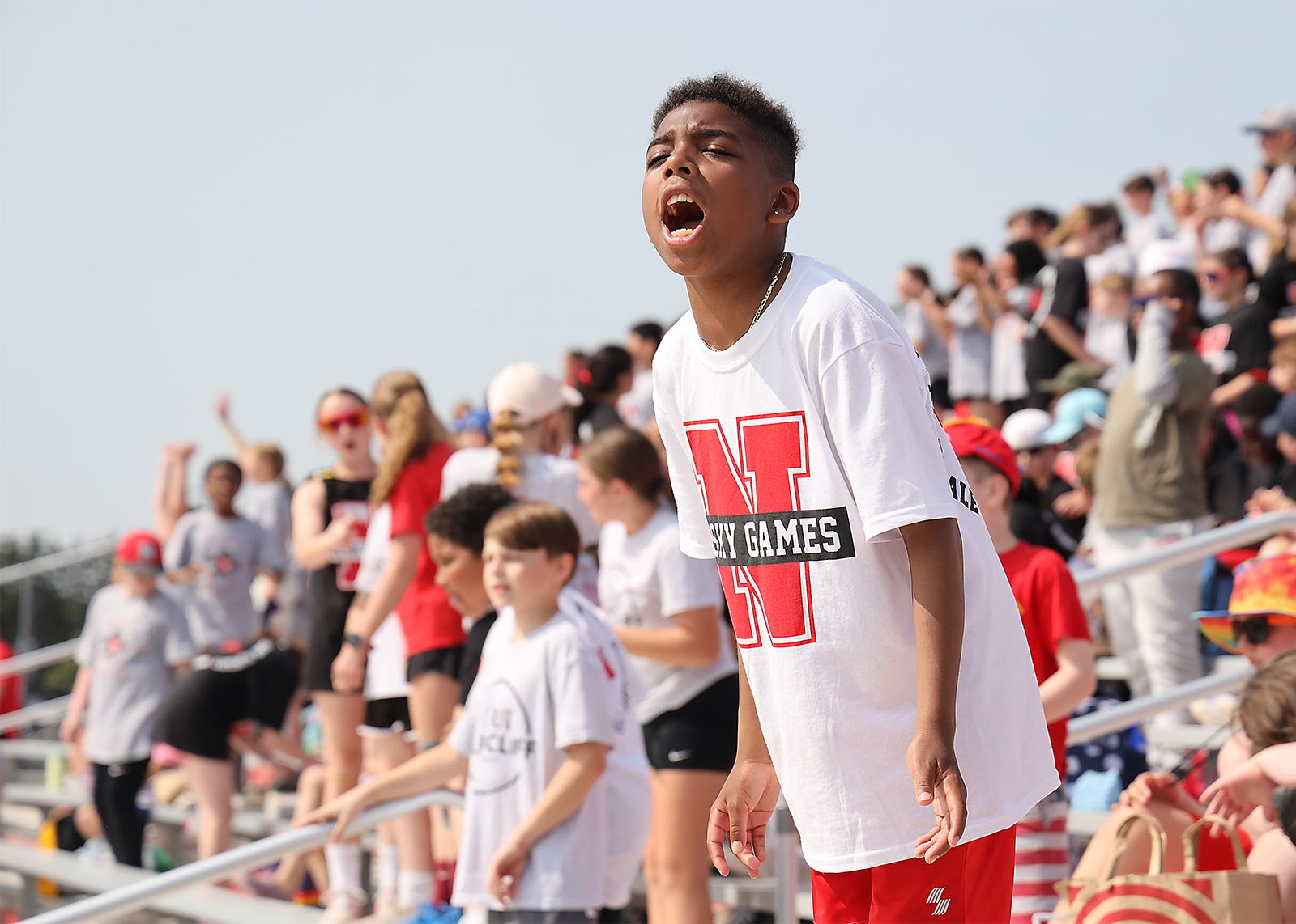 elementary student standing and cheering with students behind him in bleechers