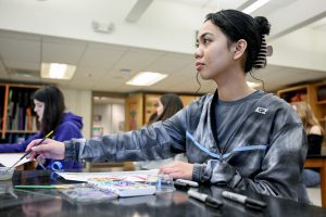 Student sitting at a desk holding a paintbrush 