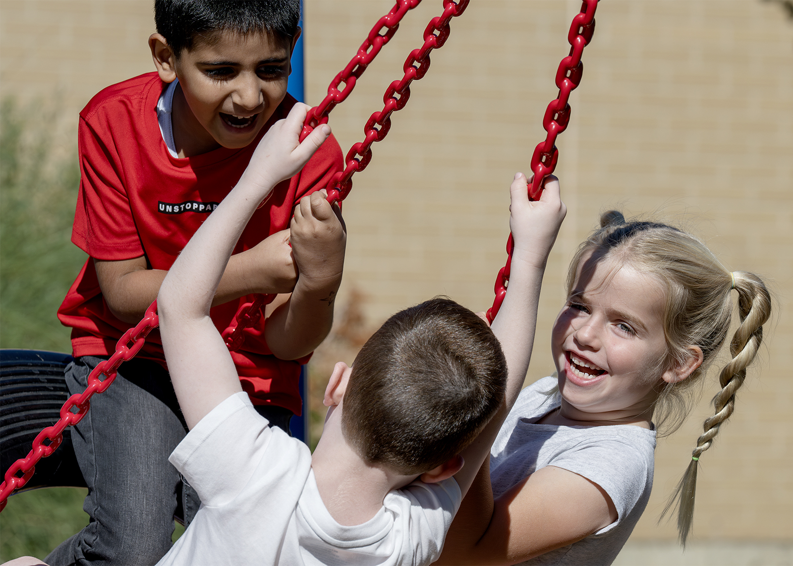 three elementary students smiling on a tire swing