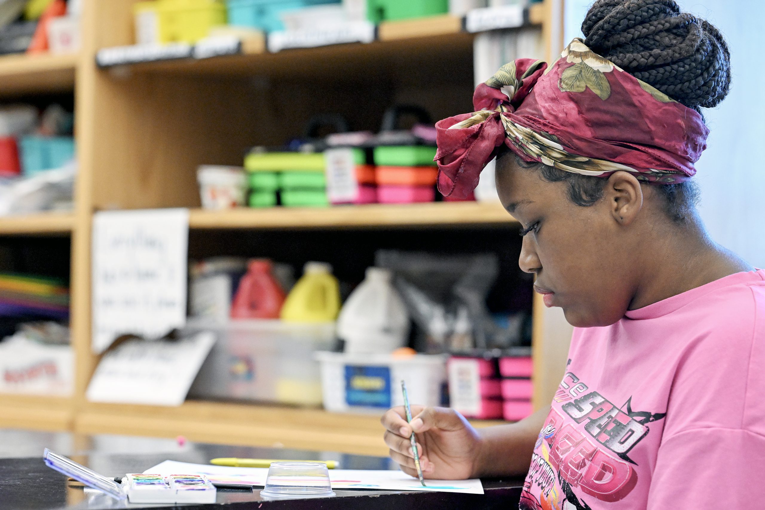 Student painting in art classroom with supplies in the background.