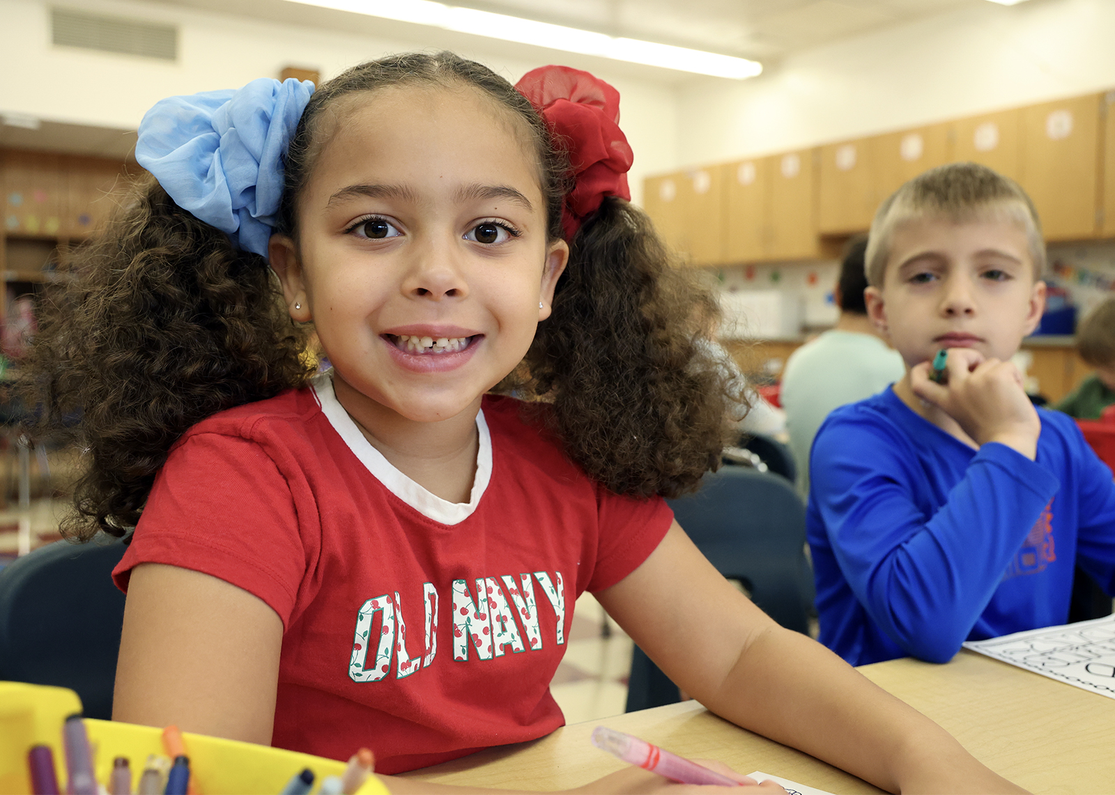 elementary student with ponytails smiles while coloring