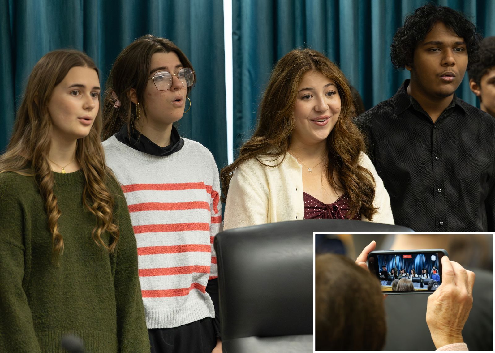 singers at town hall with inset photo of person taking a cell phone video of singers