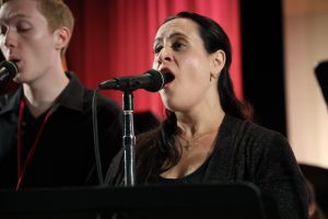 Music teacher Christina Pizzino-Catalano singing in front of a standing microphone