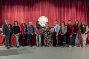Student-athlete poses with board members, some students have awards, red background.