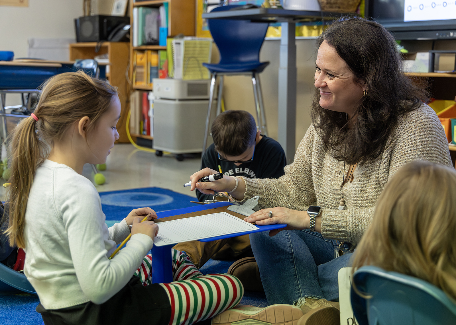 second grade teacher smiling at student sititing on floor