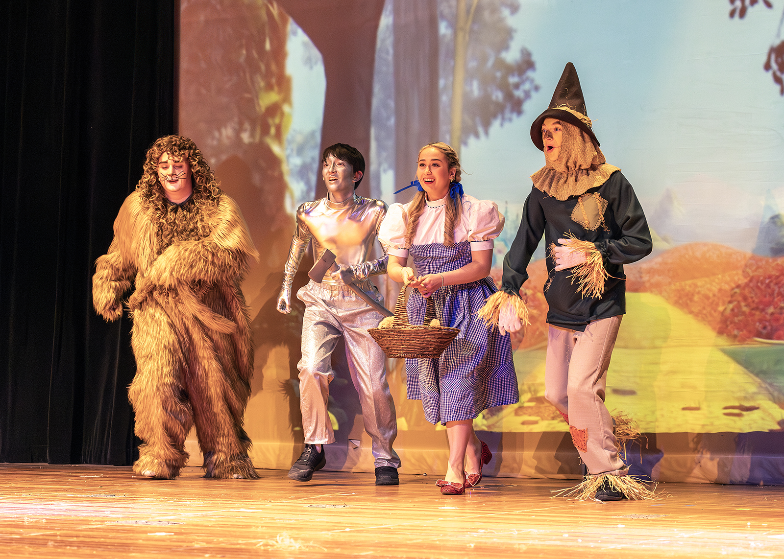 lion, scarecrow, dorothy and tin man skip on stage during play rehearsal