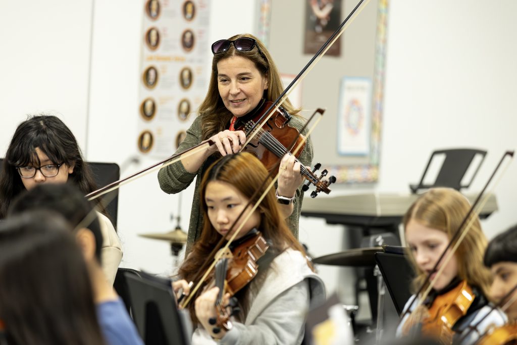 Instrumental music teacher Stacey McClenon plays violin with students in music classroom.