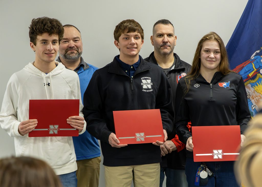 3 students holding red envelopes with 2 proud coaches behind them.