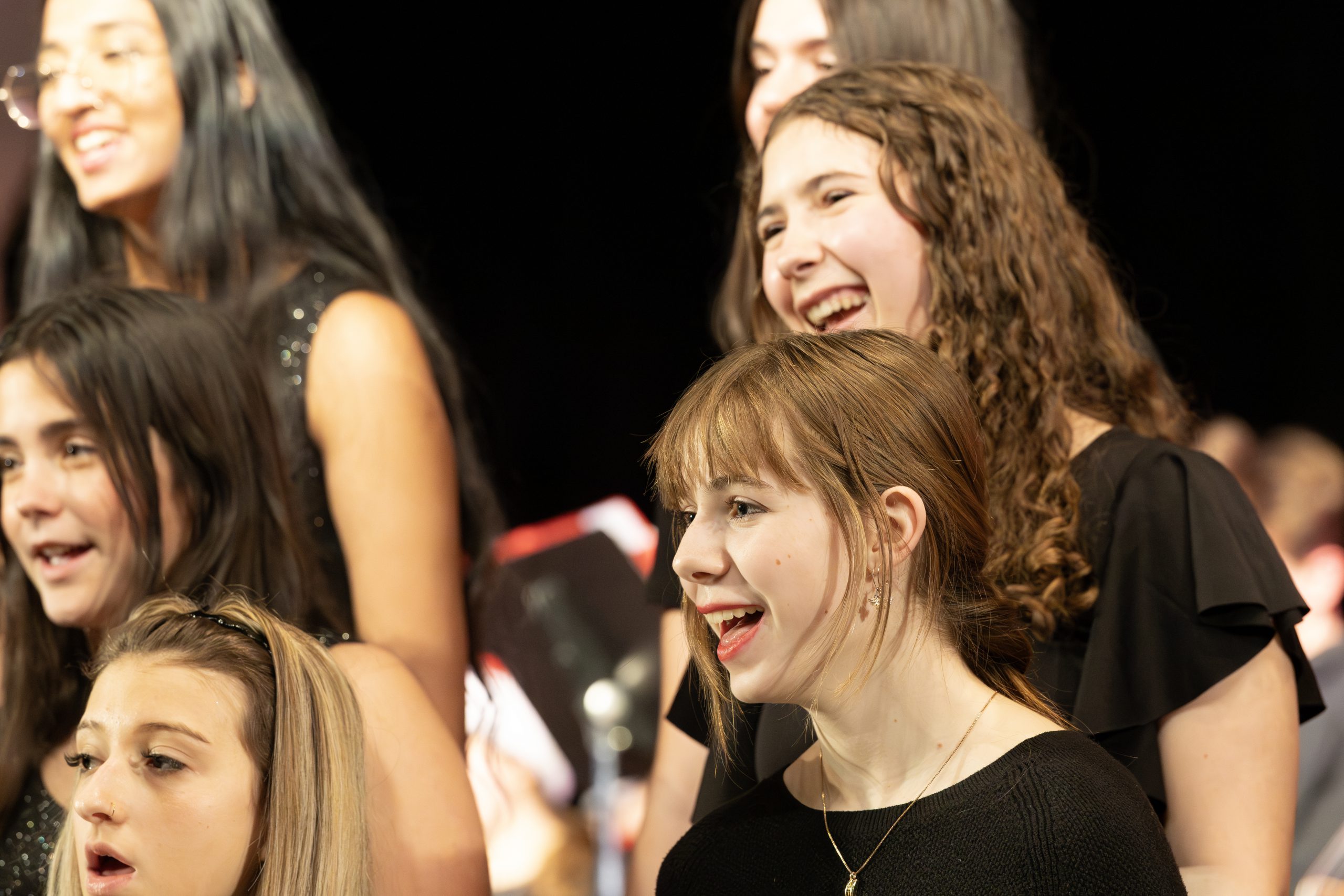 A group of students smile while singing during winter assembly performance.