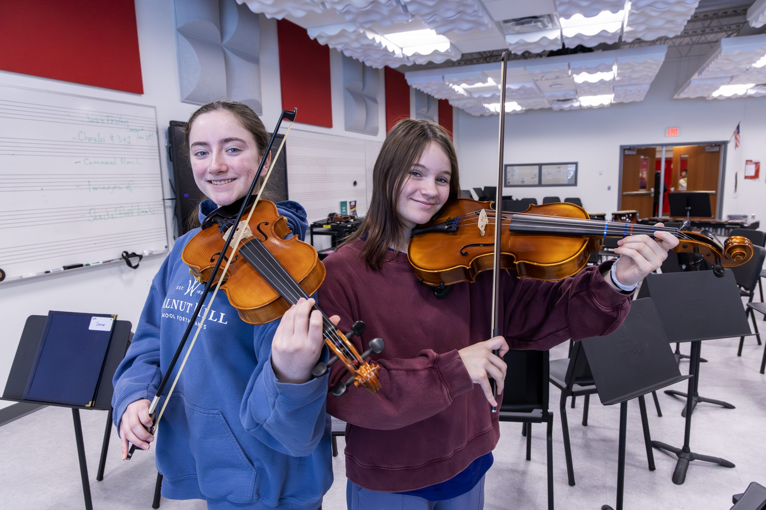 Two students hold violins in music classroom.