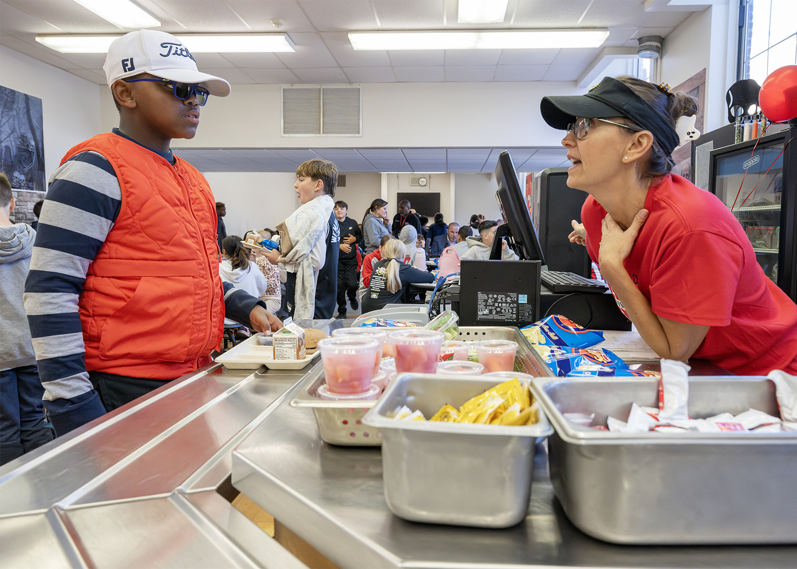 a cafeteria worker leans on counter to help student buying lunch