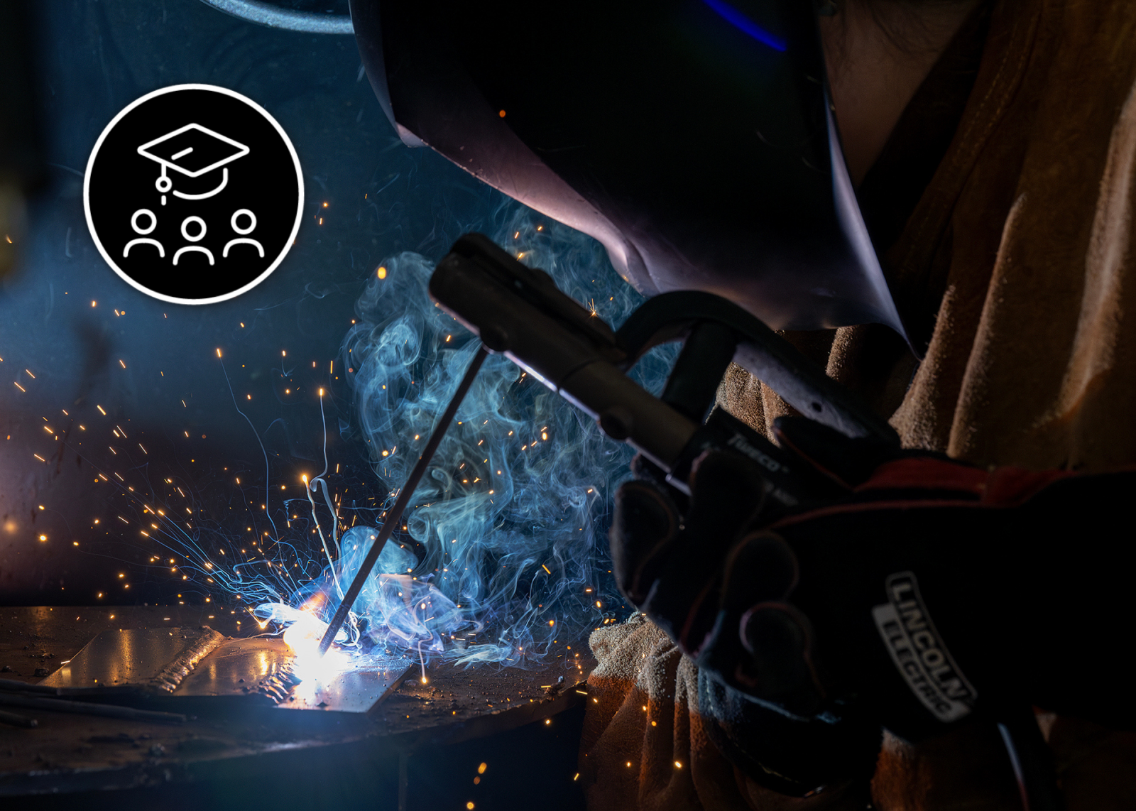 Student welding with a black circle logo in the upper lefthand cover with white line art of three people and a graduation hat.