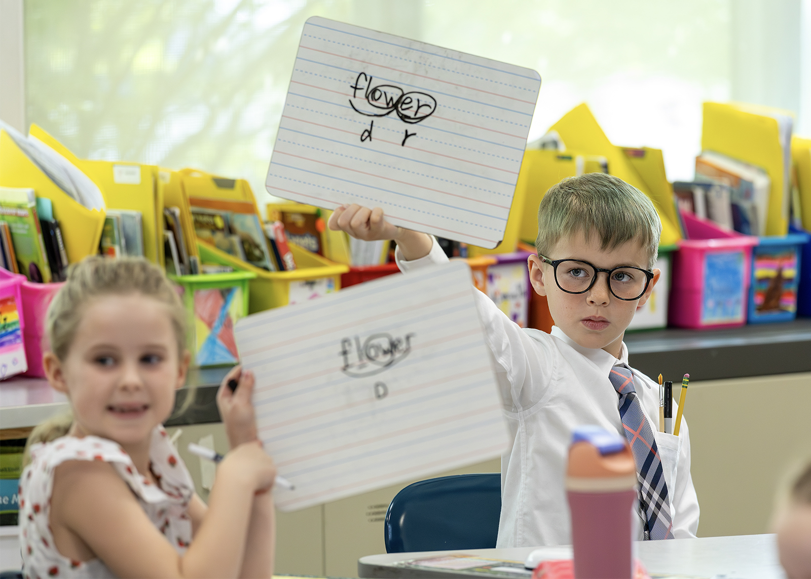 two elementary students holding up dry erase boards with ELA words