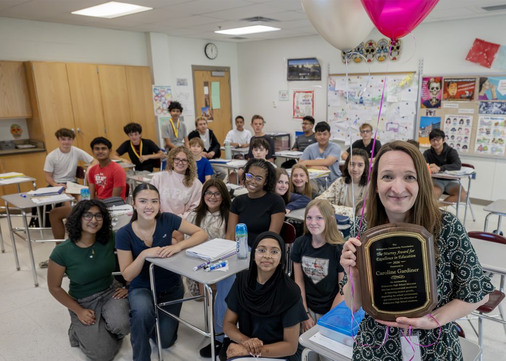 educator holding up Murray award plaque in front of classroom of kids