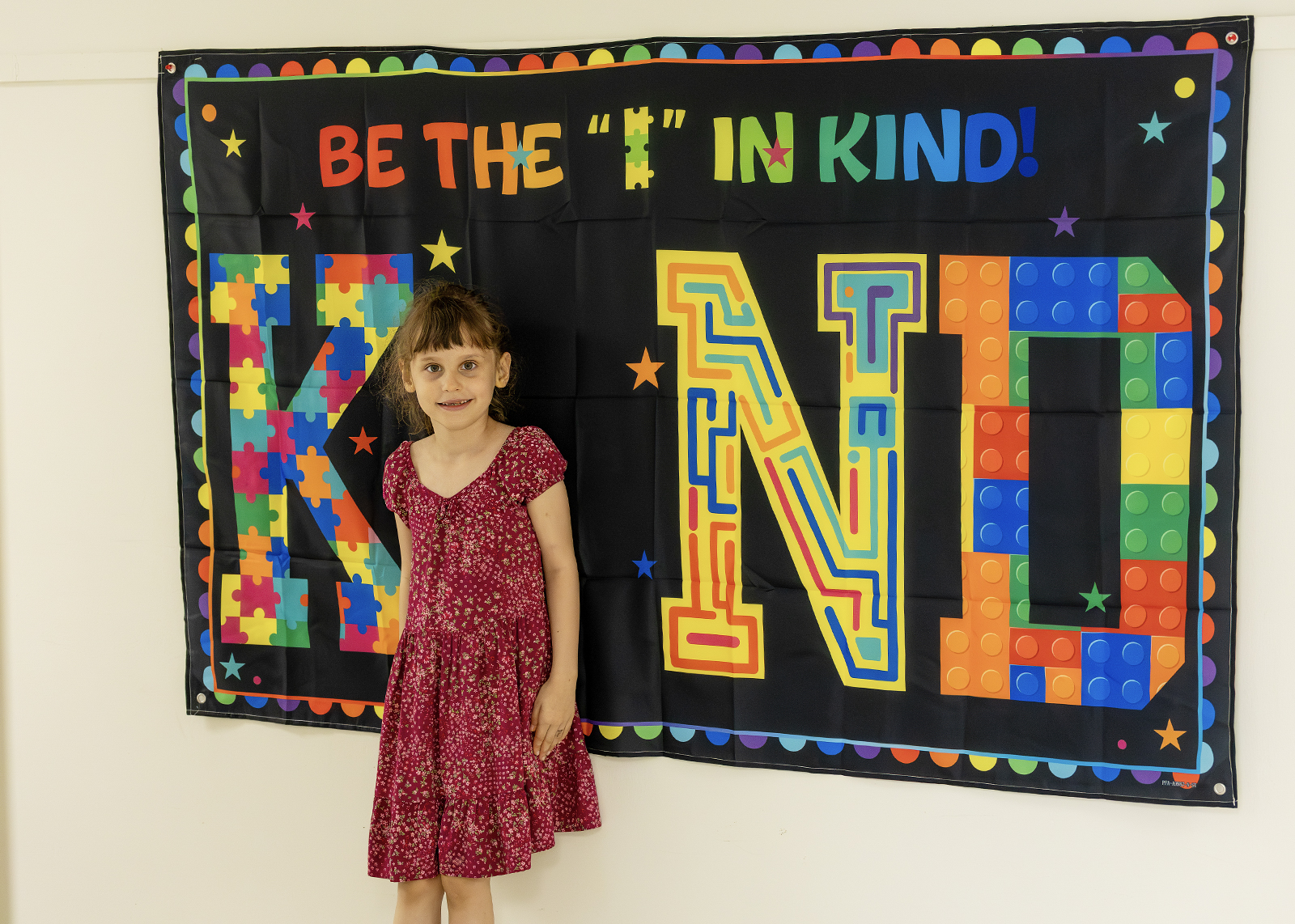 elementary student standing in front of a banner that says be the I in Kind