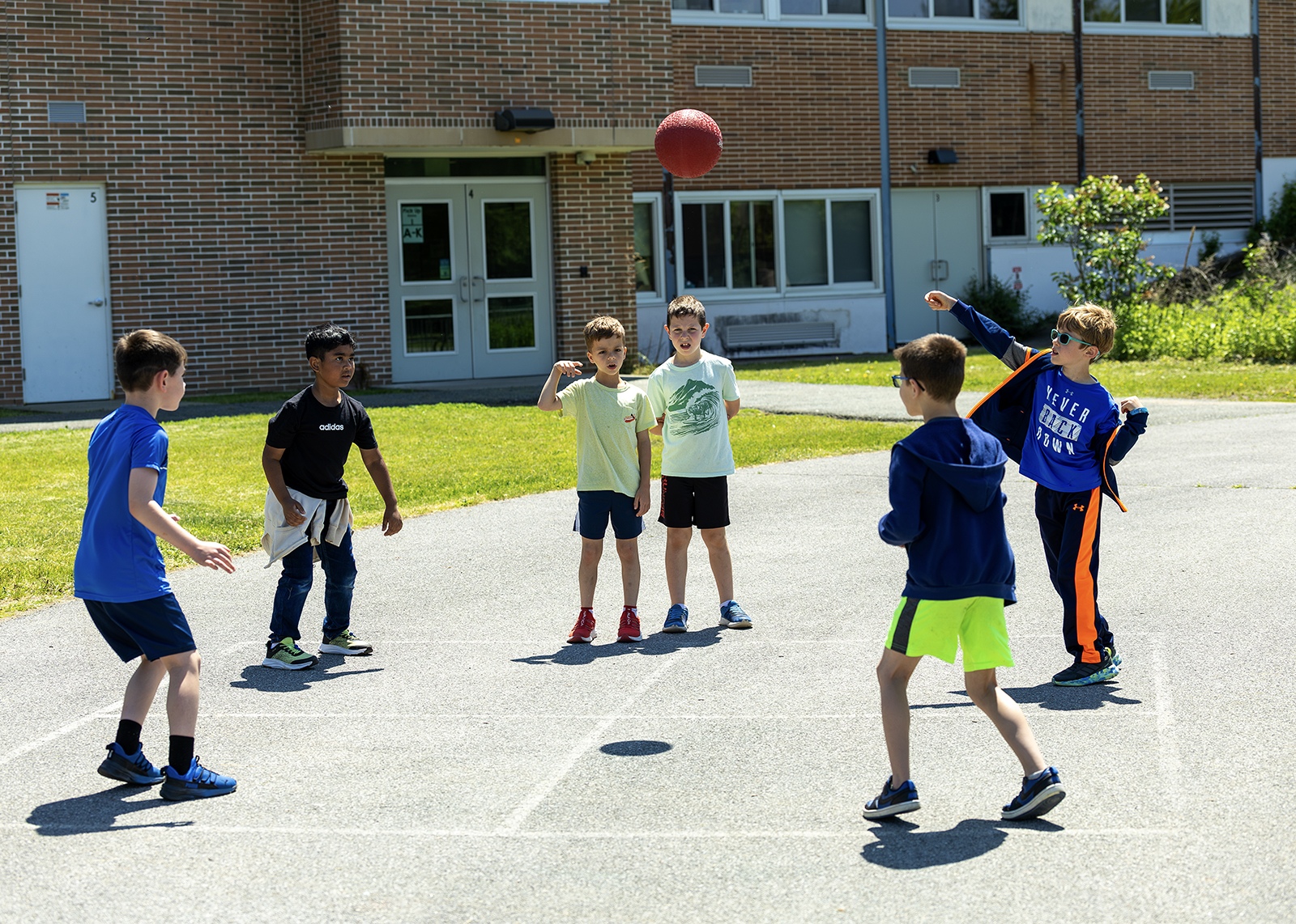 students on playground playing four square with red kickball
