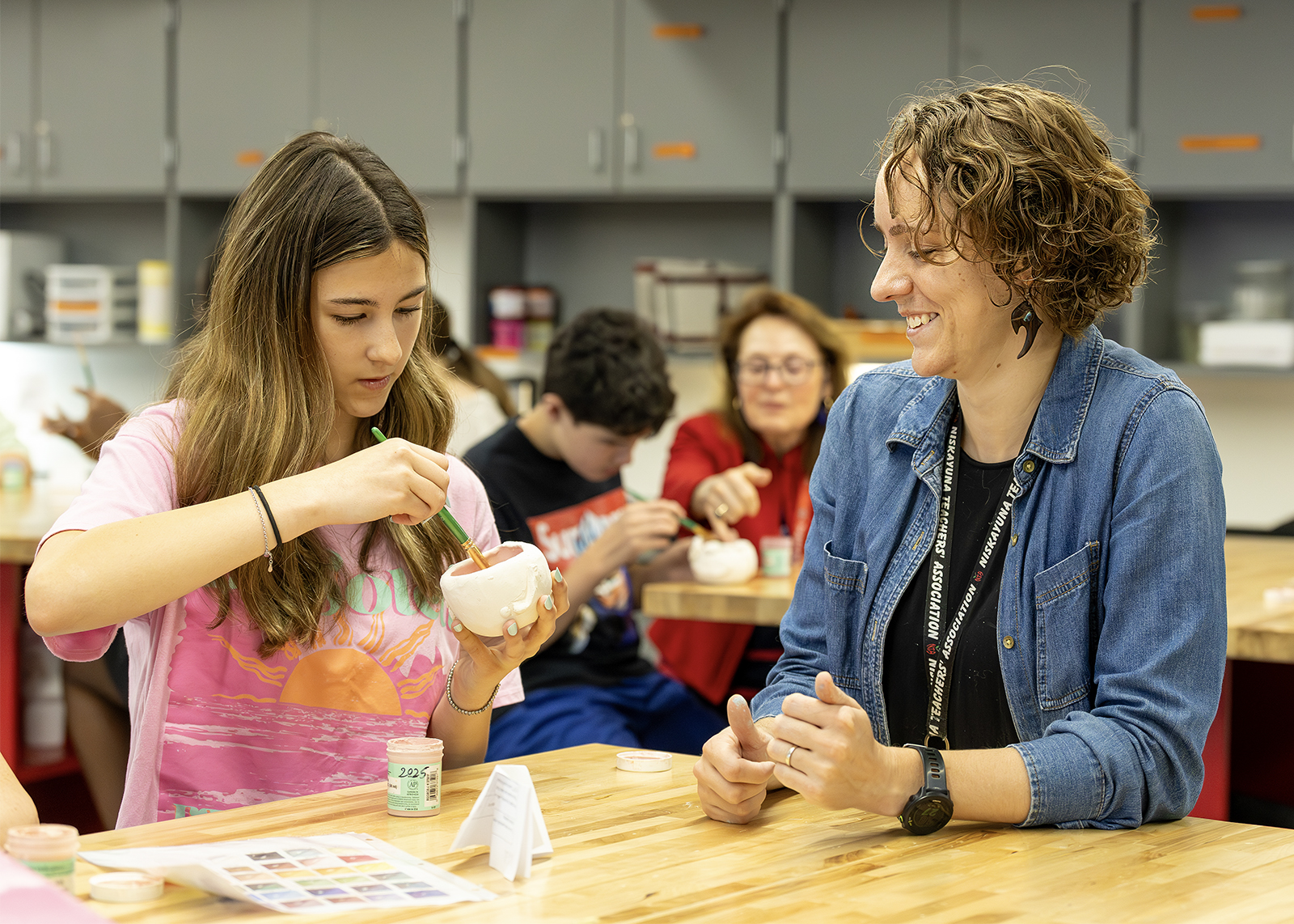 art teacher smiling with student painting a clay pot